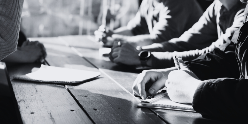 A business meeting where one man is writing notes.