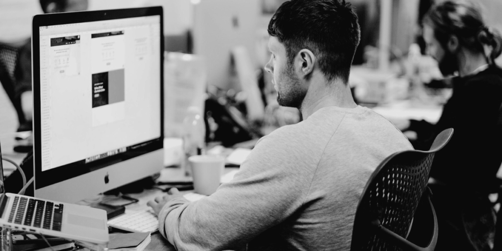 A man sitting in front of an Apple Mac desktop computer.