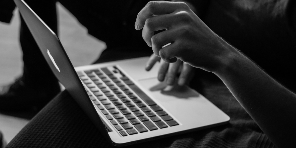 A hand using a Macbook with his left hand in the air.