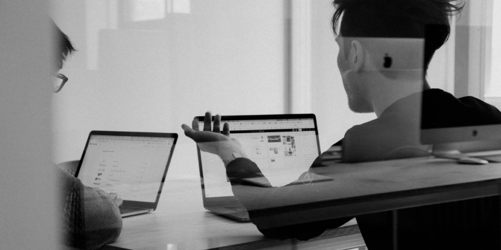 A man and coworker using their laptops at a desk.