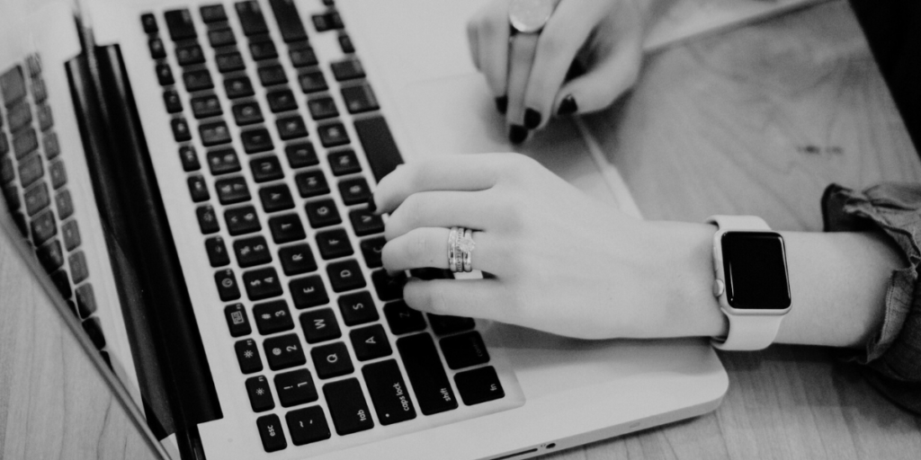 A lady with rings and a watch using a Macbook laptop.